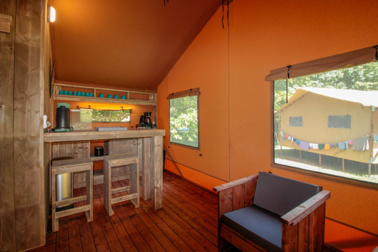 Interior de Lodgetent Brive en La Draille, Francia, con muebles de madera, cocina y grandes ventanas.