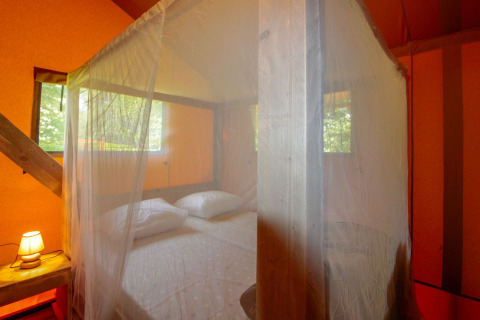 Schlafzimmer-Ambiente im Lodgetent Brive bei La Draille in Frankreich mit Moskitonetz und Bett.