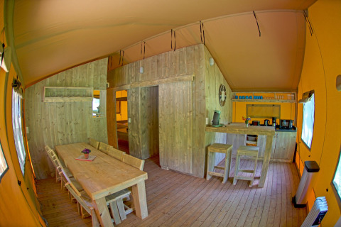 Innenansicht des Lodgetent Brive in La Draille, Frankreich, mit Essbereich, Küche und Holzmöbeln.