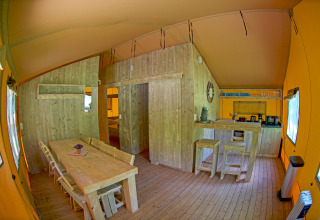 Interior view of Lodgetent Brive at La Draille in France featuring dining table, kitchen, and wood decor.