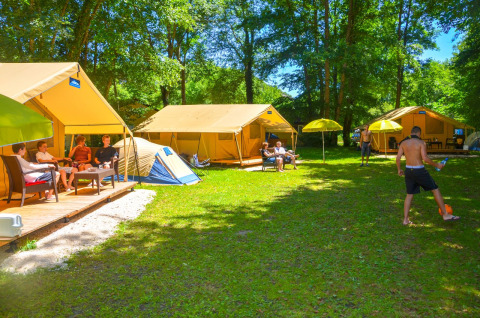 Personas relajándose y jugando balón frente a la Lodgetent St. Emilion Deluxe en el camping La Draille, Francia.