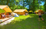 Personas relajándose y jugando balón frente a la Lodgetent St. Emilion Deluxe en el camping La Draille, Francia.