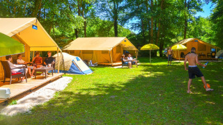 Personas relajándose y jugando balón frente a la Lodgetent St. Emilion Deluxe en el camping La Draille, Francia.