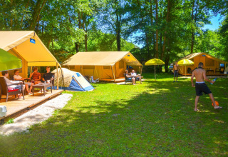 Personas relajándose y jugando balón frente a la Lodgetent St. Emilion Deluxe en el camping La Draille, Francia.