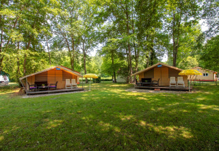 Dos tiendas safari Lodgetent St. Emilion Deluxe en La Draille, Francia, rodeadas de árboles y césped verde.