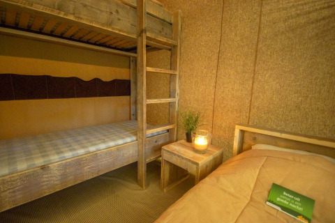 Habitación de tienda safari con litera de madera, cama individual y decoración cálida con vela encendida.