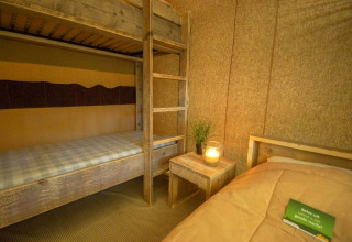Habitación de tienda safari con litera de madera, cama individual y decoración cálida con vela encendida.