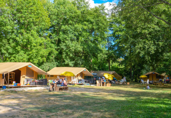 Safari-Zelte mit gelben Sonnenschirmen am Campingplatz La Draille in Frankreich, umgeben von Bäumen.