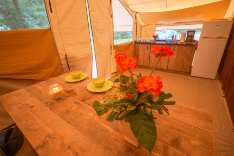Vue intérieure de la Lodgetent St. Emilion Deluxe avec fleurs, table en bois et kitchenette à La Draille, France.