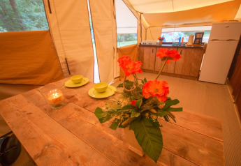 Binnenaanzicht van Lodgetent St. Emilion Deluxe met bloemen, houten tafel en keuken bij La Draille, Frankrijk.