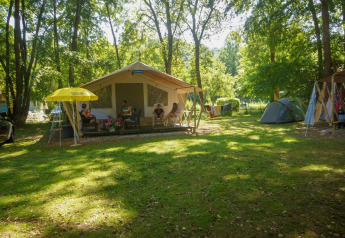 Safari lodge tent at La Draille, France, with families relaxing on the porch surrounded by trees and tents.