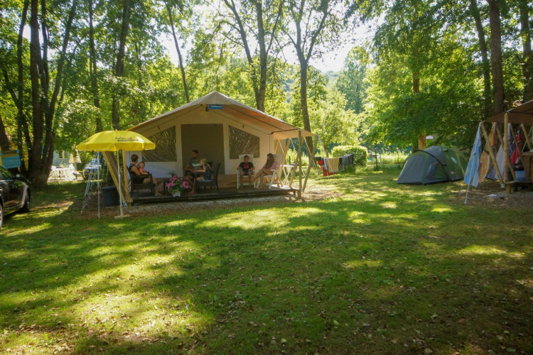 Tienda tipo safari en La Draille, Francia, con familias descansando en la terraza entre árboles y tiendas.