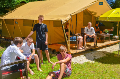 Un groupe de personnes se détend devant une tente Lodgetent St. Emilion Deluxe au camping La Draille, France.
