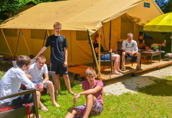 Un groupe de personnes se détend devant une tente Lodgetent St. Emilion Deluxe au camping La Draille, France.
