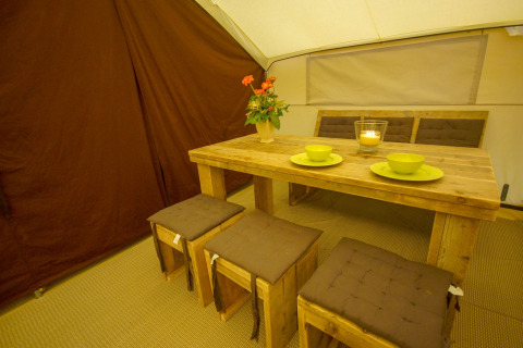 Essbereich im Lodgetent St. Emilion Deluxe, La Draille, Frankreich mit Holztisch und Hockern.