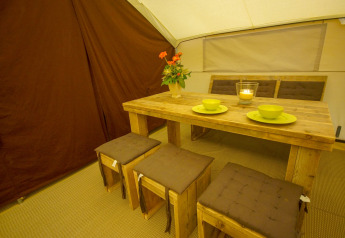 Dining area in Lodgetent St. Emilion Deluxe at La Draille, France with wooden table and stools.