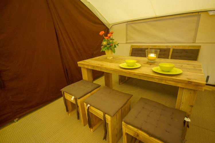 Dining area in Lodgetent St. Emilion Deluxe at La Draille, France with wooden table and stools.