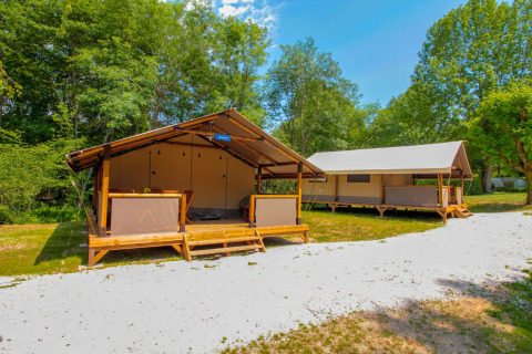 Two safari tents at La Draille in France, set among lush greenery and clear skies, perfect for glamping.