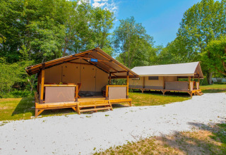 Two safari tents at La Draille in France, set among lush greenery and clear skies, perfect for glamping.