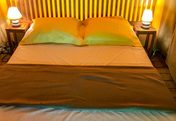 Cozy bed with wooden headboard, pillows, lamps and side tables inside the Lodgetent Gourdon safari tent in France.