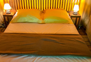 Cozy bed with wooden headboard, pillows, lamps and side tables inside the Lodgetent Gourdon safari tent in France.