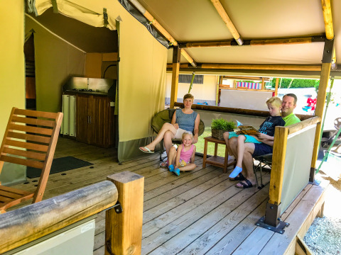 Famille détendue sur la terrasse d’une tente safari Lodgetent Gourdon au camping La Draille, France.