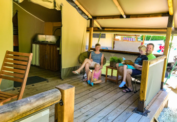 Familie slapper af på terrassen af en Lodgetent Gourdon safari-telt ved La Draille campingplads i Frankrig.