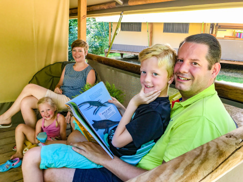 A family is smiling and relaxing together on the terrace of Lodgetent Gourdon safari tent at La Draille, France.