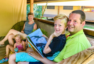 A family is smiling and relaxing together on the terrace of Lodgetent Gourdon safari tent at La Draille, France.