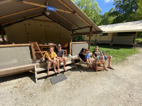 Mensen ontspannen buiten bij safaritent Lodgetent Gourdon op camping La Draille in Frankrijk, zonnige dag.