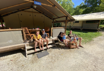 People relaxing outside the Lodgetent Gourdon safari tent at La Draille campsite in France, sunny day.