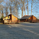 Twee houten huisjes bij River Lodge op Camping de Koeksebelt in Nederland, omgeven door bomen en gras.