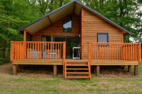 Chalet en bois au bord de la rivière avec large terrasse à Camping de Koeksebelt aux Pays-Bas, environnement vert.
