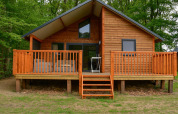 Houten lodge aan de rivier met grote veranda te midden van groen op Camping de Koeksebelt in Nederland.