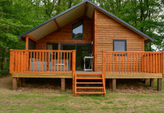 Chalet en bois au bord de la rivière avec large terrasse à Camping de Koeksebelt aux Pays-Bas, environnement vert.