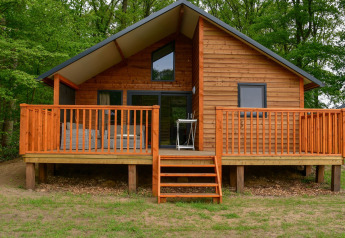 Houten lodge aan de rivier met grote veranda te midden van groen op Camping de Koeksebelt in Nederland.