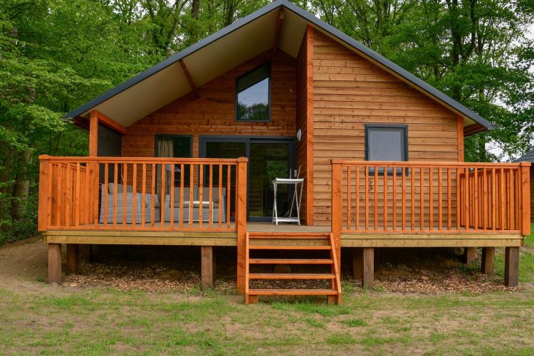Gemütliche Holzlodge am Fluss mit großer Veranda im Grünen bei Camping de Koeksebelt in den Niederlanden.