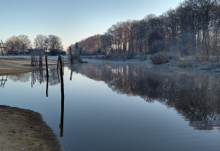Vue de la rivière à la River Lodge, Camping de Koeksebelt, Pays-Bas, avec arbres givrés et eau réfléchissante.