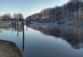 Vue de la rivière à la River Lodge, Camping de Koeksebelt, Pays-Bas, avec arbres givrés et eau réfléchissante.