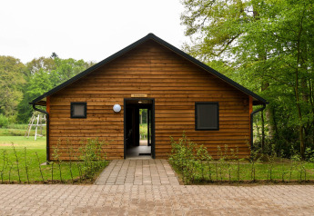 Wooden cabin at River Lodge, Camping de Koeksebelt in the Netherlands, surrounded by greenery and trees.