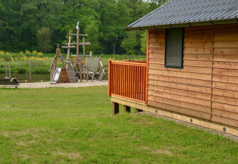 Houten lodge met speeltuin en riviertje bij Camping de Koeksebelt in Nederland, omringd door groen.