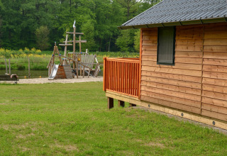 Træhytte og legeredskaber ved floden i en grøn, skovklædt campingplads ved Camping de Koeksebelt, Holland.