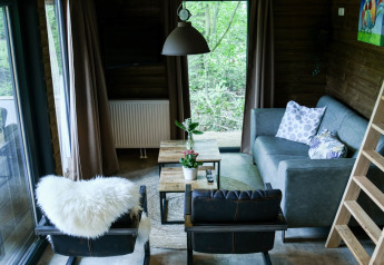 Knusse zithoek met grote ramen, grijze zetel en leren stoelen in River Lodge bij Camping de Koeksebelt.