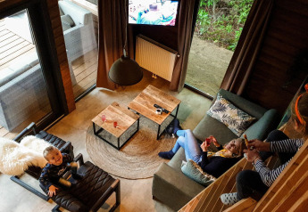 View of the living room in River Lodge at Camping de Koeksebelt, Netherlands, with a family relaxing inside.