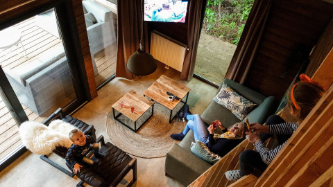 Vista de la sala de estar en River Lodge en Camping de Koeksebelt, Países Bajos, con familia relajándose.