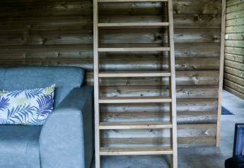 Interior de la River Lodge en Camping de Koeksebelt con escalera de madera y sofá azul con cojín.