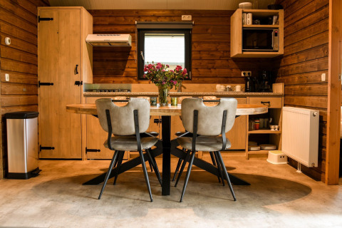 Moderne lodgekøkken ved River Lodge på Camping de Koeksebelt, med trævægge og spisebord med blomster.