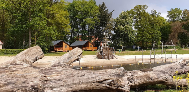 Bild vom River Lodge bei Camping de Koeksebelt in den Niederlanden mit Holzhütten, Strand und Spielplatz.