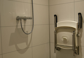 Shower area with foldable seat and support handles on the wall at River Lodge, Camping de Koeksebelt, Netherlands.