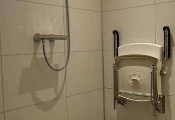 Douche met opklapbare stoel en steunhandgrepen aan de muur bij River Lodge, Camping de Koeksebelt, Nederland.